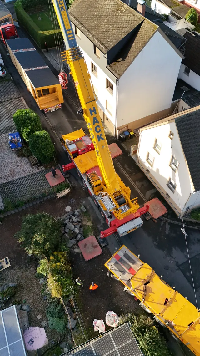 Kranfahrzeug hebt ein vorgefertigtes Modulhaus-Element bei der Montage auf dem Grundstück an