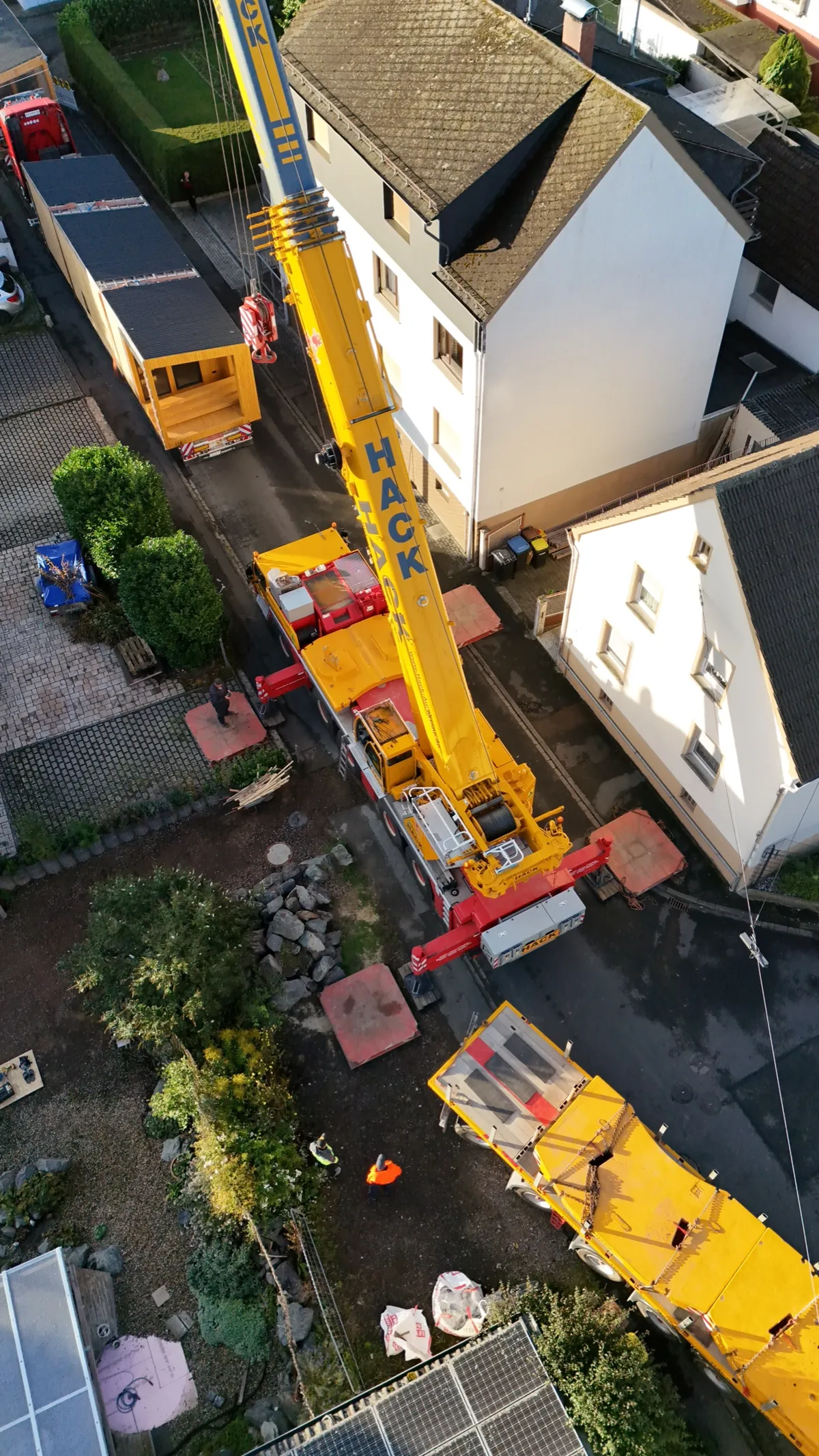 Kranfahrzeug hebt ein vorgefertigtes Modulhaus-Element bei der Montage auf dem Grundstück an